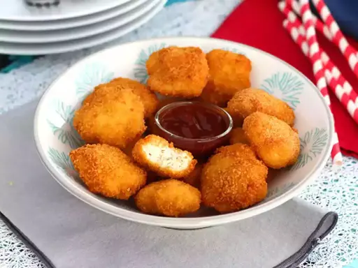 Un plato lleno de crujientes nuggets caseros, listos para mojar en salsa barbacoa.