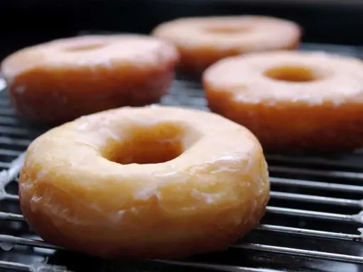 Cuatro donuts glaseados sobre una rejilla, listos para disfrutar. Una deliciosa receta de donuts caseros.