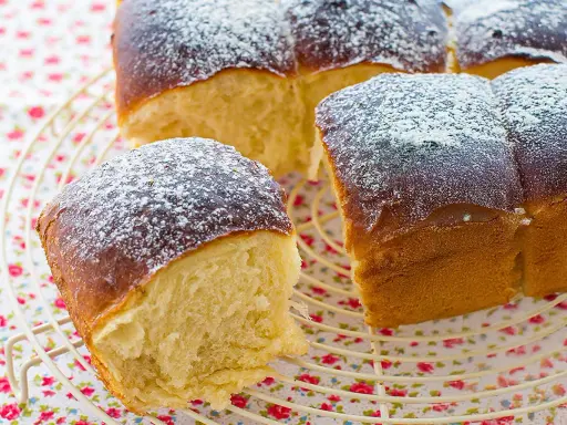 Pan brioche esponjoso y dorado, espolvoreado con azúcar glas sobre una rejilla.