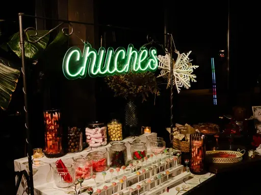 Una mesa de chuches para una boda rústica, con un letrero de neón "Chuchés", frascos de dulces, piruletas y decoración invernal.