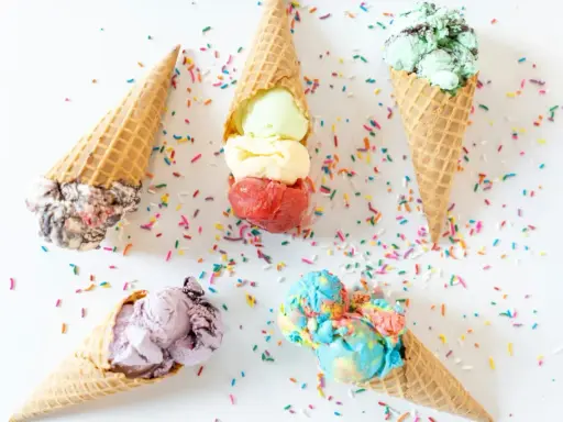Cinco conos de helado de chuche de colores vibrantes, esparcidos con confeti sobre fondo blanco.