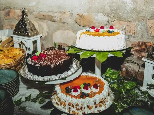 Mesa dulce boda casera con tres pasteles decorados con frutas y chocolate. Hay también cestas con patatas fritas y adornos rústicos.