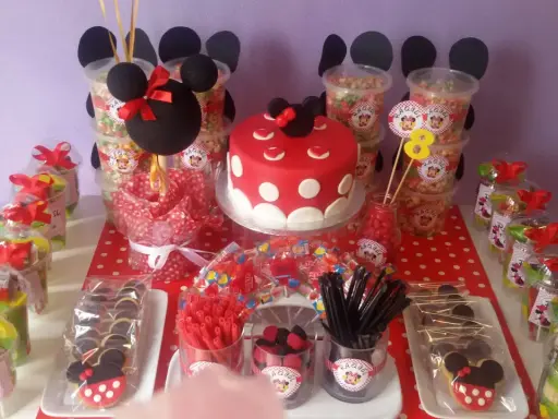 Mesa de fiesta temática de Minnie Mouse con pastel, galletas, palomitas y muchos centros de chuches para niños.
