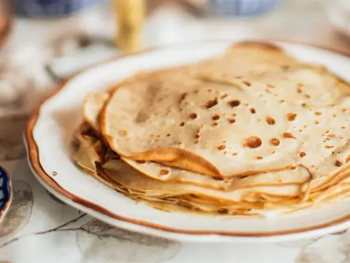 Una pila de masa crepes doradas y finas en un plato blanco.