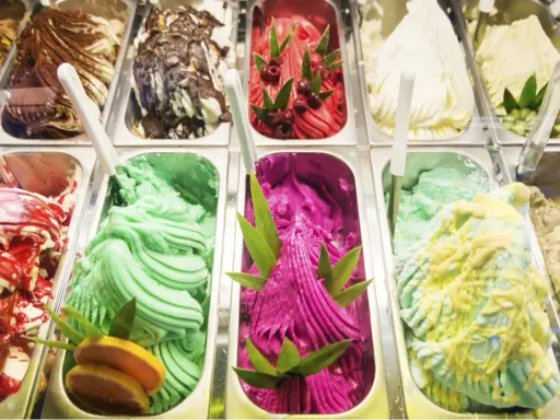 Variedad de helados cremosos, incluyendo un vibrante helado de pitahaya con azúcar invertida, decorado con hojas verdes y frutos rojos.