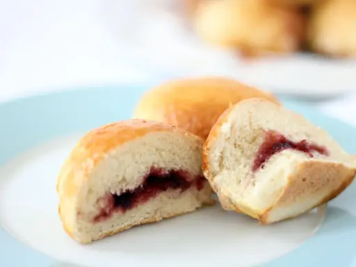 Dos bollos dorados, uno cortado, revelan un relleno de mermelada de fresa. ¡Un dulce bocado!