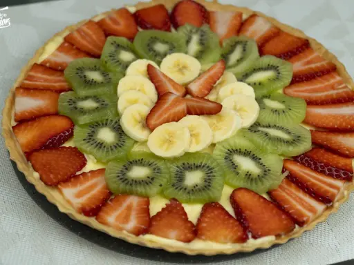 Deliciosa tarta con decoración de tartas con frutas: fresas, kiwi y plátano, dispuestas en círculos concéntricos sobre una base cremosa.