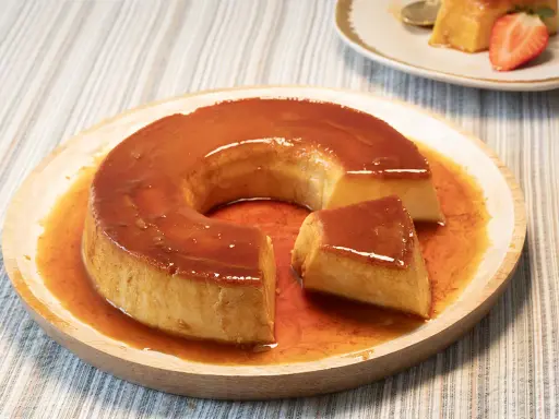 Un delicioso flan de leche condensada con caramelo líquido, servido en un plato de madera.