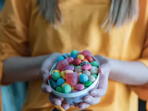 Manos sostienen un cuenco lleno de chuches saludables para niños: gomitas de corazón, bolitas de colores y más.