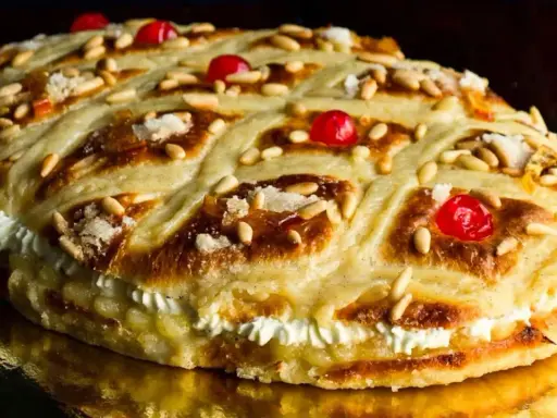 Deliciosa coca de Sant Joan rellena de crema, decorada con piñones, cerezas rojas y azúcar.