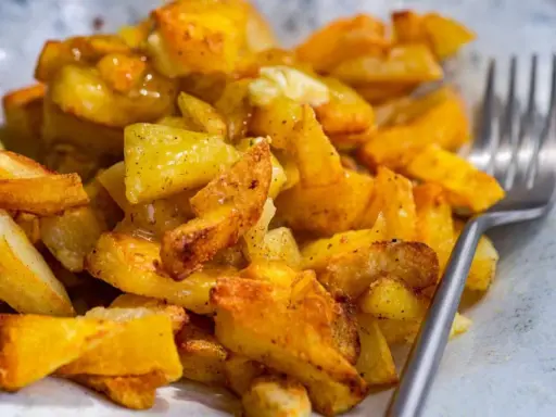 Patatas fritas al horno doradas y crujientes, sazonadas con especias, listas para disfrutar con un tenedor.