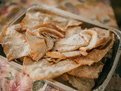 Orejas de carnaval espolvoreadas con azúcar glas en una bandeja metálica. ¡Perfectas para tu receta!