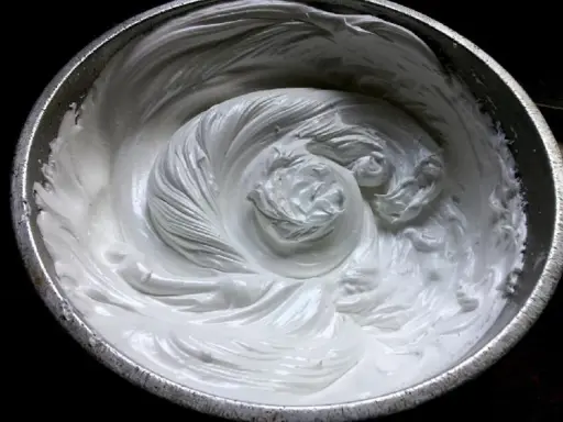 Merengue italiano recién batido en un bol metálico, con remolinos suaves y sedosos que invitan a probar su dulzura.