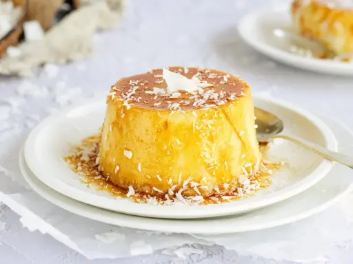 Delicioso flan de coco con caramelo líquido y coco rallado, servido en un plato blanco con una cuchara dorada.