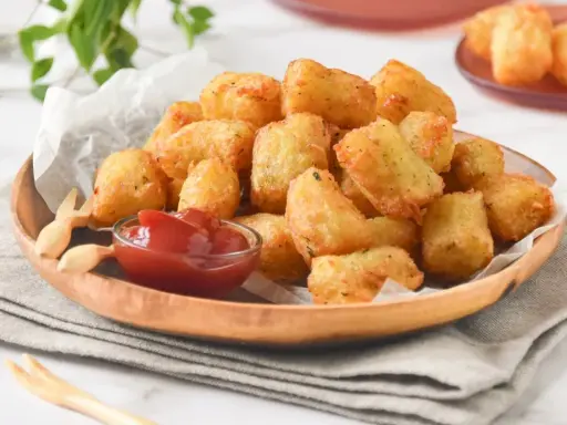 Tater tots dorados y crujientes servidos en un plato de madera con ketchup.