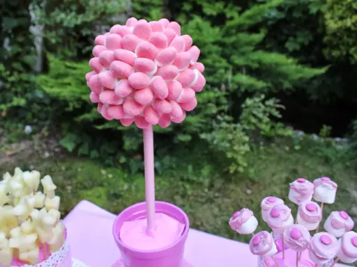 Un árbol de gominolas rosa, decorado con dulces, preside una mesa de fiesta al aire libre.