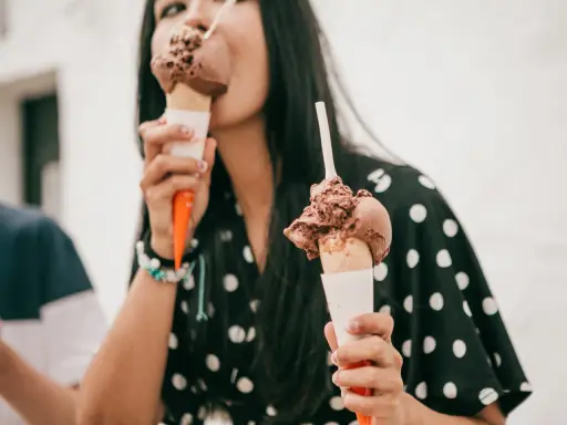 Una mujer disfruta de dos helados de chocolate, preguntándose quién inventó esta delicia.
