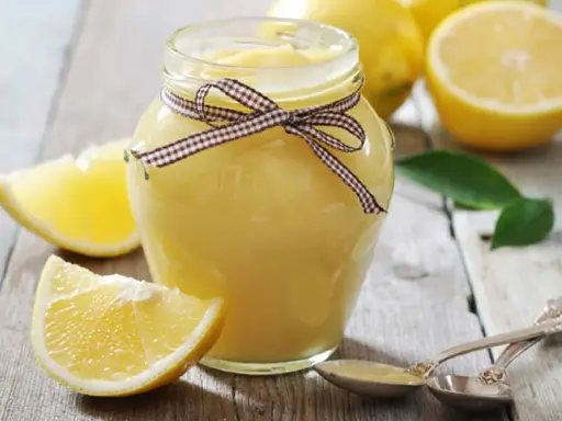 Tarro de lemon curd casero, decorado con un lazo, rodeado de limones frescos y rodajas.