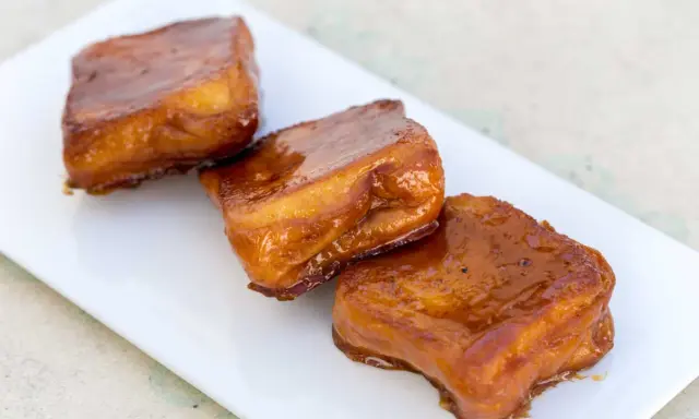 Tres torrijas de miel, doradas y brillantes, reposan en un plato blanco.