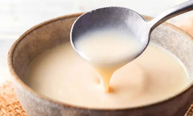Cuchara sirviendo crema inglesa espesa y suave en un cuenco rústico.