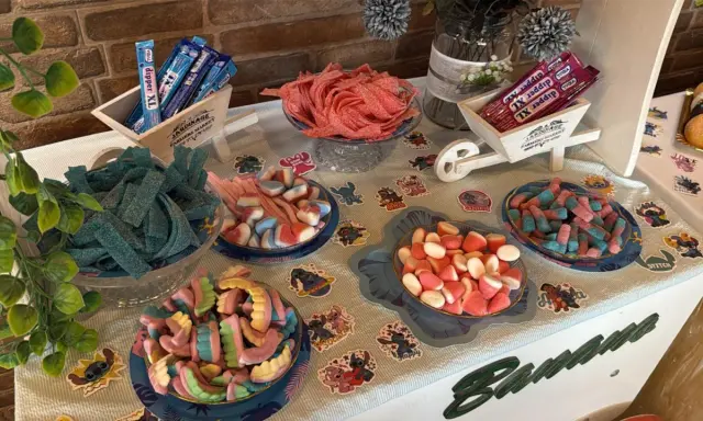 Una mesa llena de todas las chuches del mundo: gominolas azules, rojas, rosas y de muchos colores, dispuestas en cuencos y carretillas.