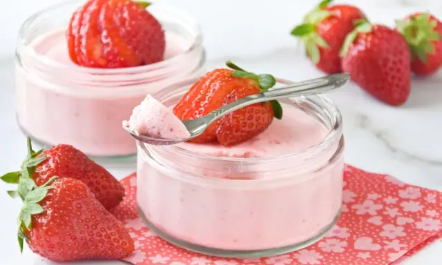Delicioso postre con fresas, cremoso y ligero, servido en frascos de vidrio. Una fresa fresca corona cada porción.
