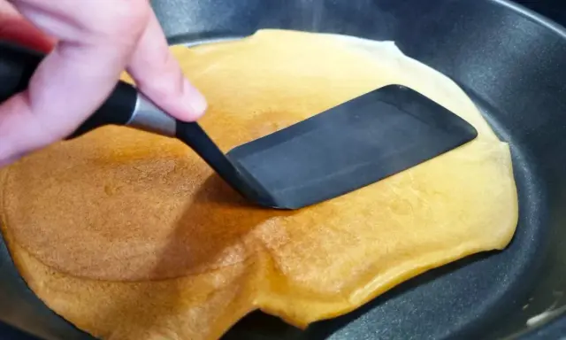 Volteando un crepé dorado en una sartén, preparado fácilmente con crepes thermomix.