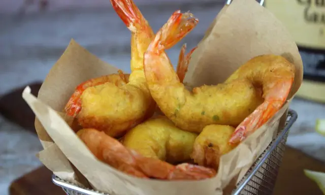Crujientes gambas a la gabardina doradas, servidas en una cesta metálica con papel marrón.