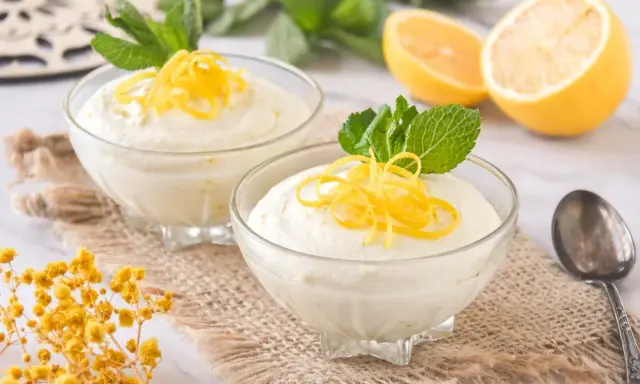 Dos copas de cremoso mousse de limón con leche condensada, decoradas con ralladura de limón y menta.