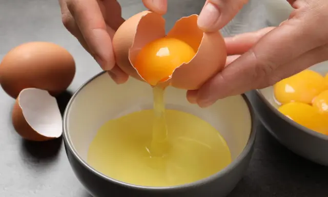 Manos separando la yema de la clara de un huevo. Ideas para saber qué hacer con claras de huevo y yemas.