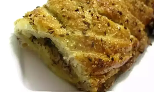Deliciosa trenza de hojaldre dorada, espolvoreada con azúcar y semillas, lista para disfrutar.