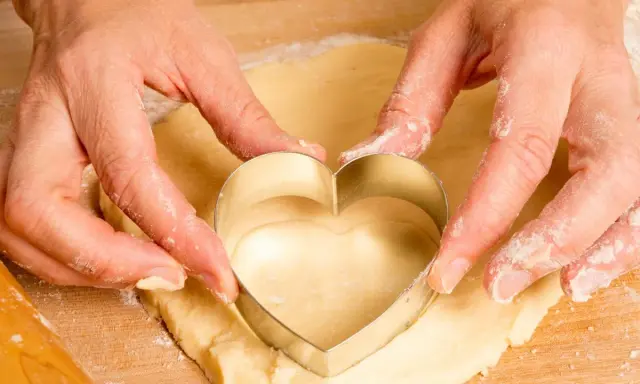 Manos cortan masa con un cortador en forma de corazón, parte de una receta de galletas caseras.