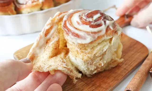 Un rollo de canela esponjoso, cubierto de glaseado cremoso, se separa suavemente.