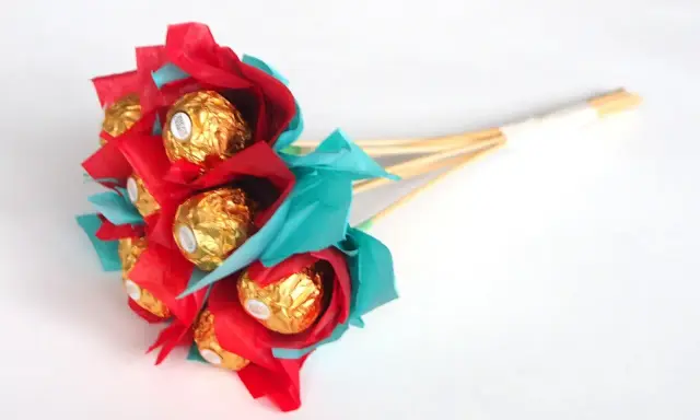 Un ramo de bombones dorados envueltos en papel rojo y turquesa, ideal para un regalo dulce y original.