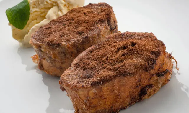 Dos torrijas de chocolate espolvoreadas con cacao y azúcar, acompañadas de helado de vainilla y una hoja de menta.