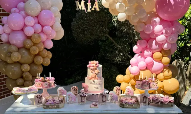 Mesa dulce baby shower con pastel de osito, galletas temáticas y globos rosas y dorados. ¡Bienvenida Mia!