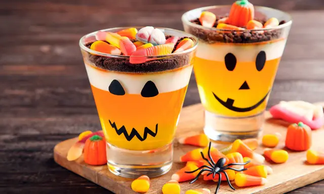 Deliciosa gelatina Halloween para niños, con capas de naranja y blanco, decorada como calabaza y cubierta de dulces.
