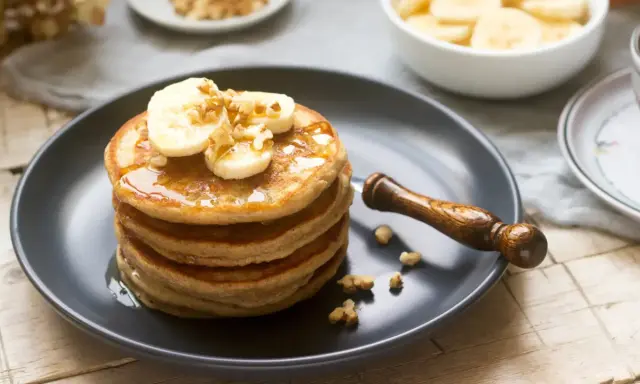 Pila de tortitas americanas con plátano y nueces, bañadas en sirope. Un desayuno perfecto.