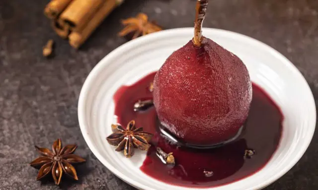 Peras al vino tinto, cocidas con especias como anís estrellado y canela, servidas en un plato blanco con su sirope.