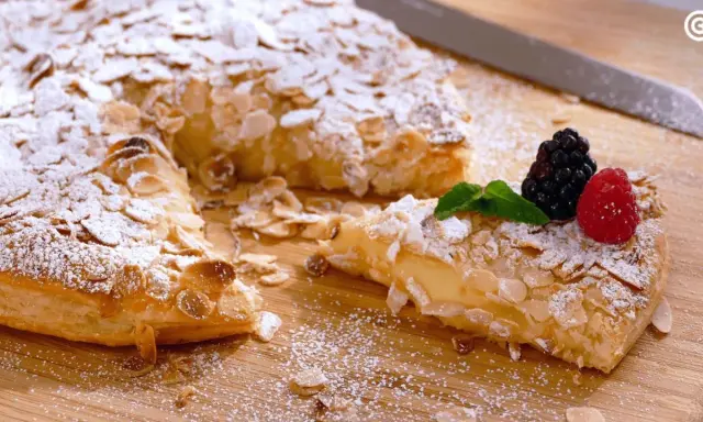 Deliciosos postres con hojaldre, cubiertos de almendras laminadas y azúcar glas. Una porción muestra un relleno cremoso y frutos rojos.