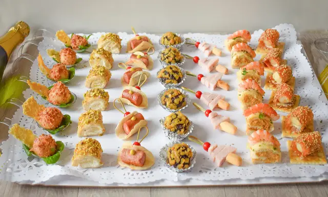 Bandeja con variedad de bocaditos salados, perfectos para un picoteo fácil y económico. Hay mini tacos, bolitas cubiertas de frutos secos, brochetas de jamón y canapés con gambas y salmón.