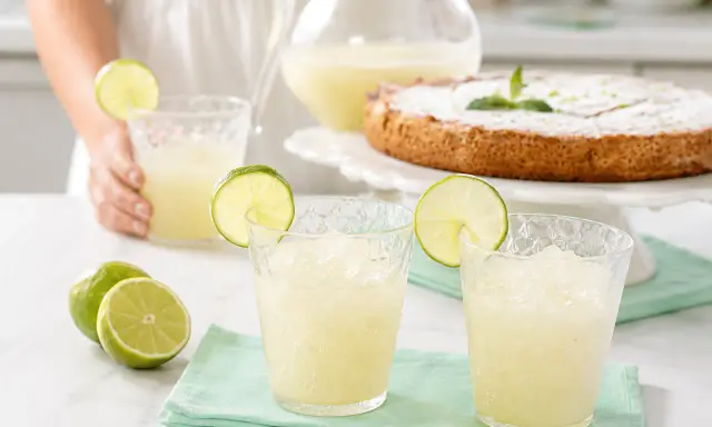 Refrescante granizado de limón Thermomix, perfecto para un día caluroso. Servido en vasos con rodajas de lima y acompañado de un delicioso pastel.