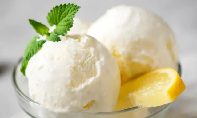 Delicioso helado de limón casero en copa de cristal, adornado con menta fresca y rodajas de limón.
