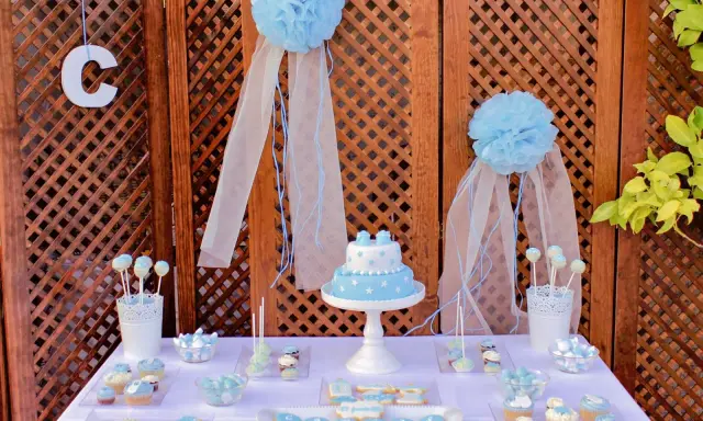 Mesa dulce bautizo casera con pastel, galletas y cupcakes decorados en tonos azules.
