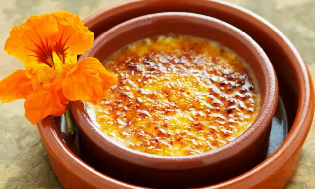 Crema catalana con una flor naranja. El postre tiene una capa de azúcar caramelizado crujiente.