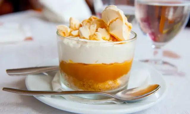 Postre en vaso con capas de galleta, crema y mermelada de mango, coronado con merengue crujiente, como un polvito canario.
