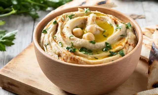Hummus cremoso en cuenco de madera, decorado con garbanzos, aceite de oliva y perejil. Perfecto para aprender como hacer hummus casero.