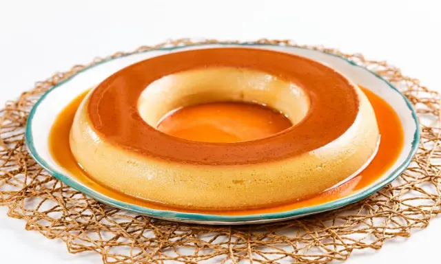 Un delicioso flan de café, con su caramelo dorado, reposa en un plato blanco con borde azul, sobre una esterilla tejida.