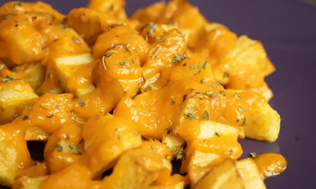Patatas bravas receta: patatas fritas crujientes cubiertas con una salsa brava cremosa y hierbas picadas.