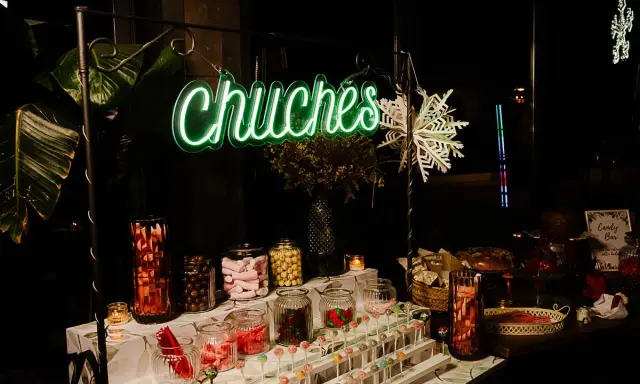 Una mesa de chuches para una boda rústica, con un letrero de neón "Chuchés", frascos de dulces, piruletas y decoración invernal.